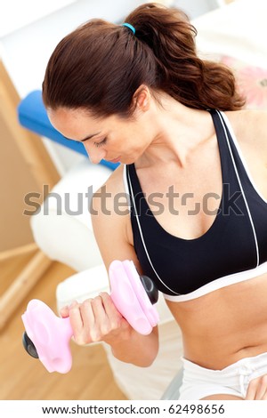 Athletic hispanic woman holding a dumbbell in her living-room at home
