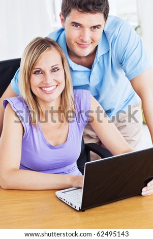 Smiling couple using computer on the desk looking at the camera