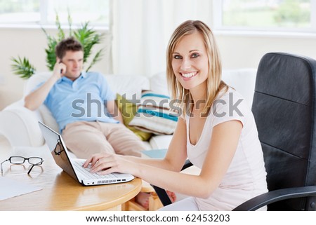 Beautiful couple with woman using laptop and man having a call sitting on a sofa in their living-room