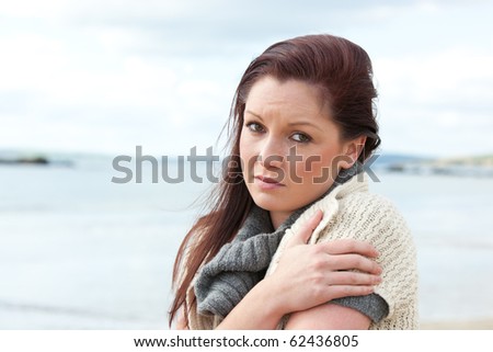 Unhappy woman wearing hat and scarf on the beach
