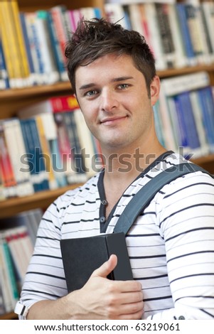 Portrait of a smart student holding a book standing in the library of his university