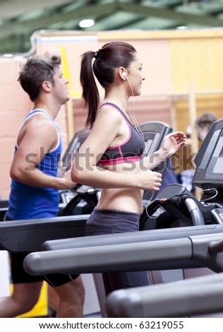 Pretty woman with earphones using a treadmill with her boyfriend in a fitness centre