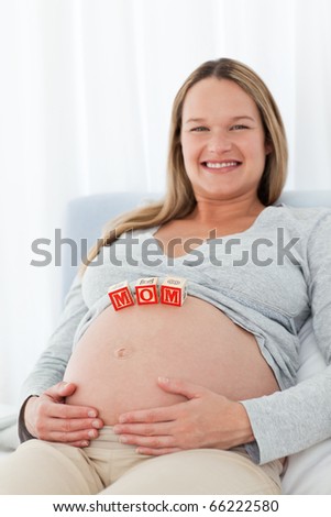 Adorable woman with mom letters on the belly while relaxing on a bed