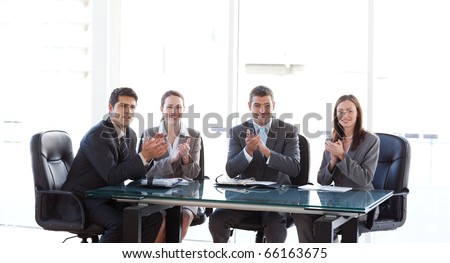 Cheerful businessteam applauding during a presentation sitting around a table