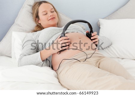Happy future mom putting headphones on her belly lying on a bed