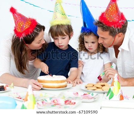 Cute little boy cutting a birthday cake for his family in the kitchen