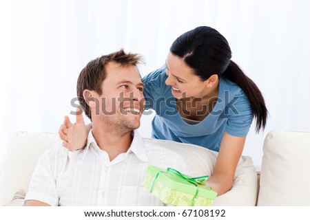 Happy man receiving a present from his girlfriend while sitting on the sofa