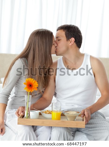 Happy woman kissing her boyfriend for bringing the breakfast in the bedroom
