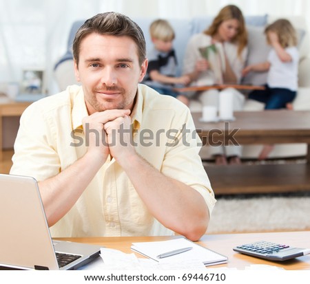 Man calculating his bills while his family are on the sofa