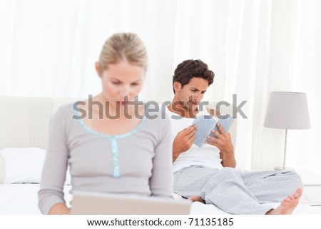 Woman working on her laptop while her husband is reading at home