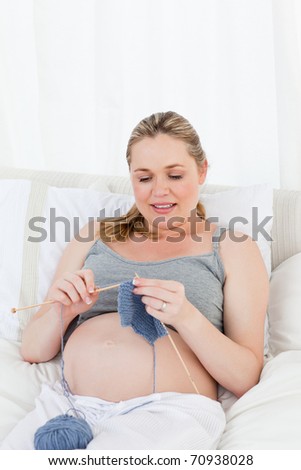 Adorable pregnant woman knitting on her bed at home