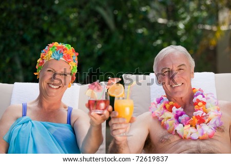 Mature couple drinking a cocktail  beside the swimming pool at home