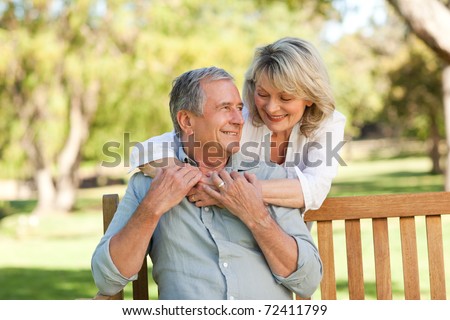 Senior woman hugging her husband who is on the bench