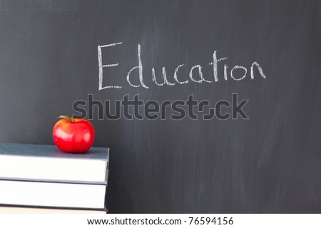 Stack of books with a red apple and a blackboard with 