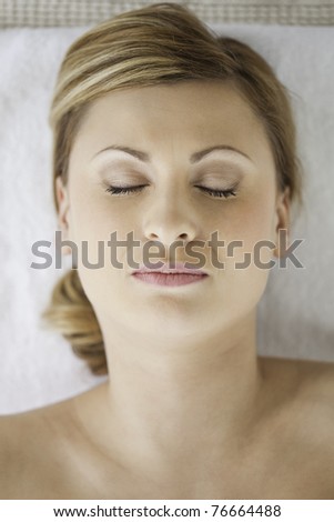 Young and pretty blond-haired woman lying down while receiving a spa treatment