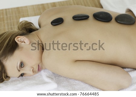 Cute blond-haired woman lying down with stones on her back in a spa centre