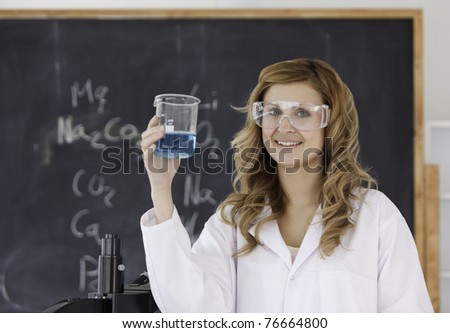 Cute scientist looking at the camera holding a blue beaker