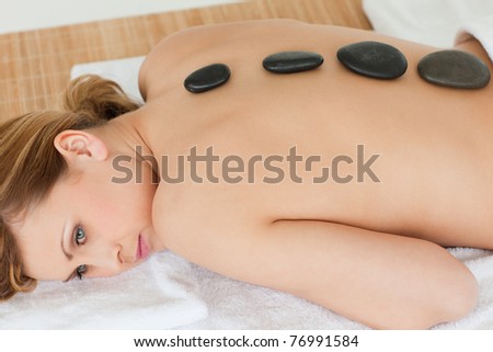 Cute blond-haired woman lying down with stones on her back in a spa center