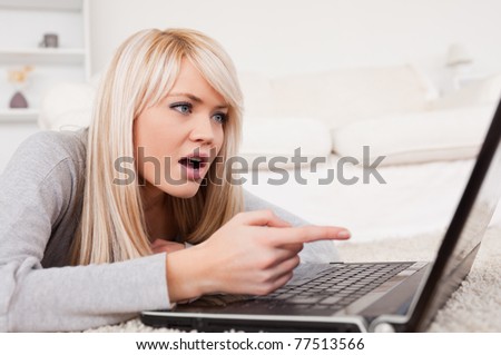 Pretty blond woman frustrated with her computer lying on a carpet in the living room