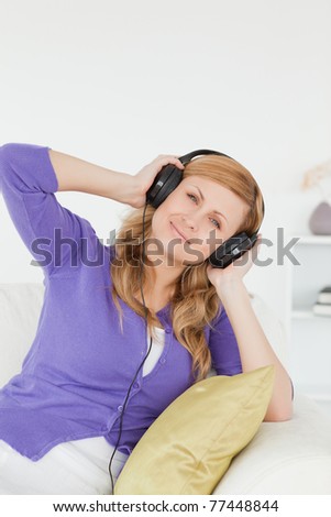 Good looking red-haired woman listening to music and enjoying the moment while sitting on a sofa in the living room