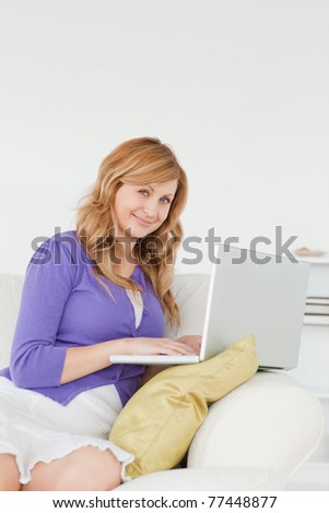 Attractive red-haired woman sitting on the sofa and using a laptop in her apartment