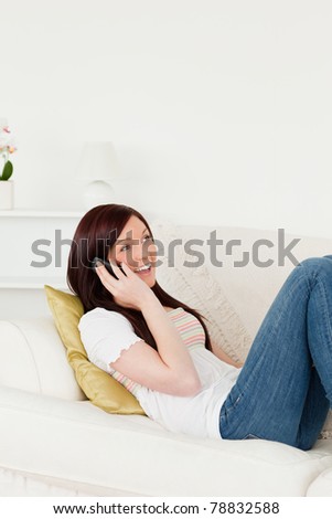 Pretty red-haired woman having a conversation on the phone while lying on a sofa in the living room