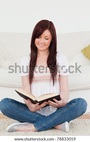 Attractive red-haired woman reading a book while sitting on a sofa in the living room