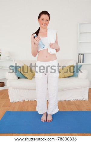 Smiling female having a rest after stretching while standing on a gym carpet in the living room