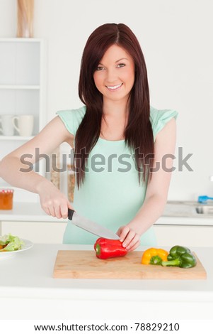 Good looking red-haired woman cutting some vegetables in the kitchen in her apartment