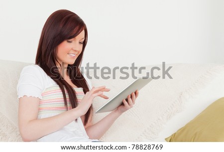 Good looking red-haired woman relaxing with her tablet while sitting on a sofa in the living room
