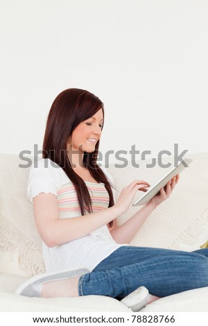 Beautiful red-haired woman relaxing with her tablet while sitting on a sofa in the living room