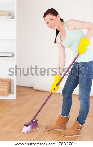 Good looking red-haired woman sweeping the floor at home