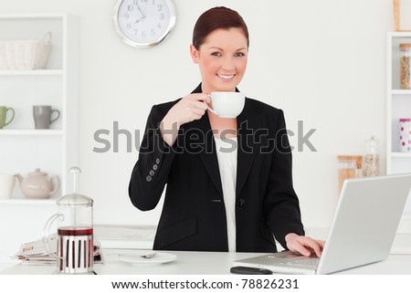 Pretty red-haired woman in suit relaxing with her laptop in the kitchen in her appartment