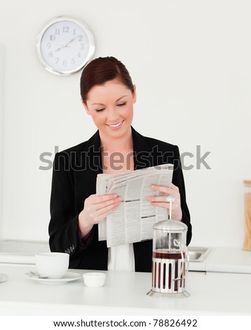 Good looking red-haired woman in suit reading the newspaper in the kitchen in her apartment