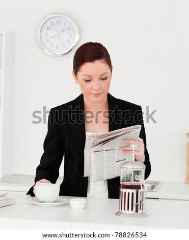 Pretty red-haired woman in suit reading the newspaper in the kitchen in her apartment
