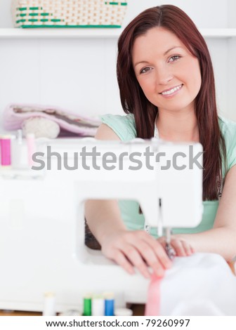 Attractive red-haired woman using a sewing machine in her living room
