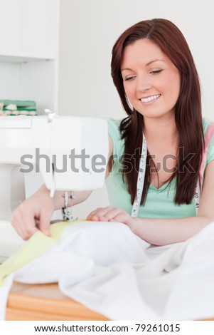 Cute red-haired female using a sewing machine in her living room