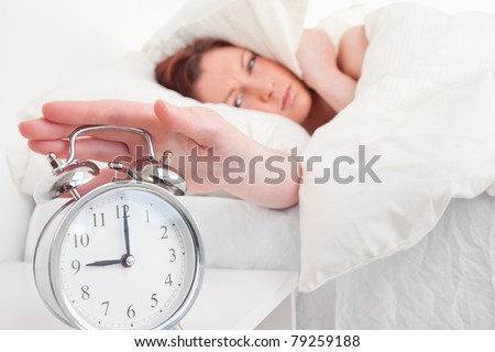 Gorgeous red-haired female waking up thanks to an alarm clock in the bedroom