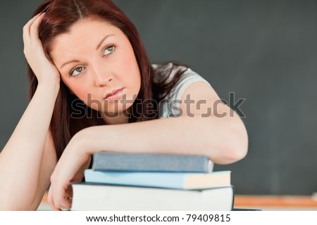 Close up of a beautiful bored student with her forearm on her books in a classroom