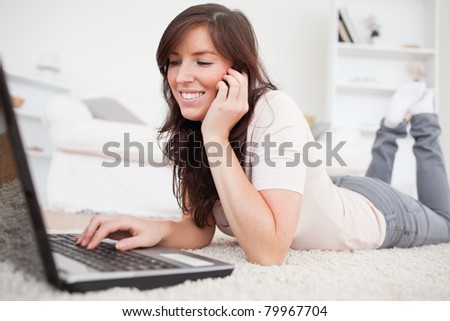 Attractive brunette woman on the phone while relaxing with her laptop in the living room