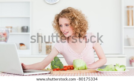 Good looking blonde woman relaxing with her laptop while cooking some vegetables in the kitchen in her apartment