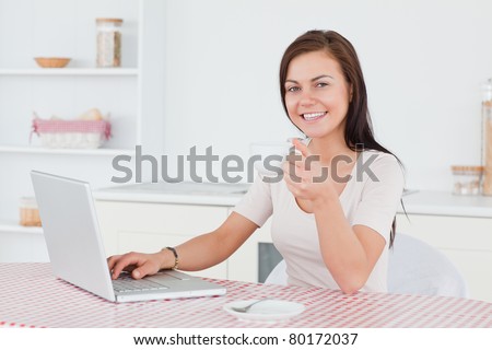 Charming brunette using her laptop and having a tea in her kitchen