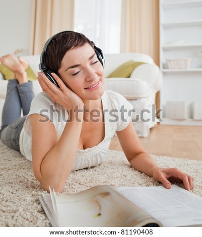 Portrait of a delighted woman with a magazine enjoying some music while lying on a carpet