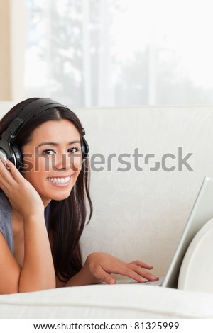 charming woman with earphones lying on sofa smiling into camera in living room