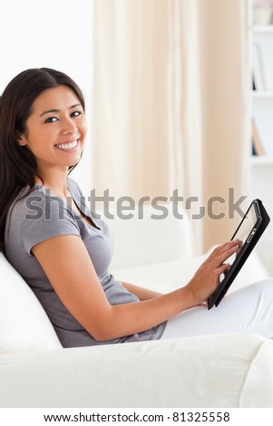 smiling woman sitting on sofa with tablet looking into camera in living room