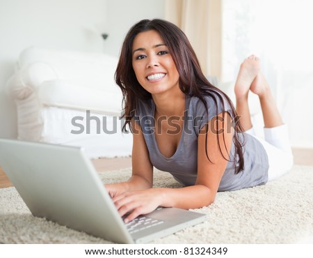 happy woman lying on a carpet with notebook smiling into camera in living room