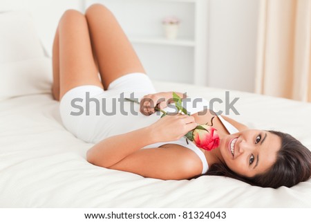 good-looking woman with rose lying on bed looking into camera in bedroom