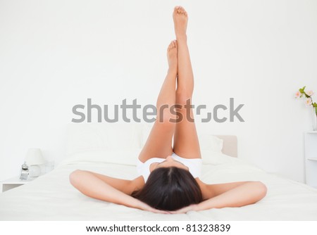 beautiful woman legs raised up high and arms under her head lying on bed in bedroom