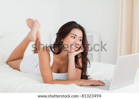 charming woman lying on bed in bedroom with crossed legs and laptop