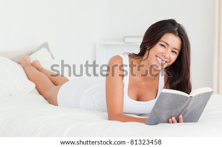 dark-haired woman lying on bed with book in bedroom